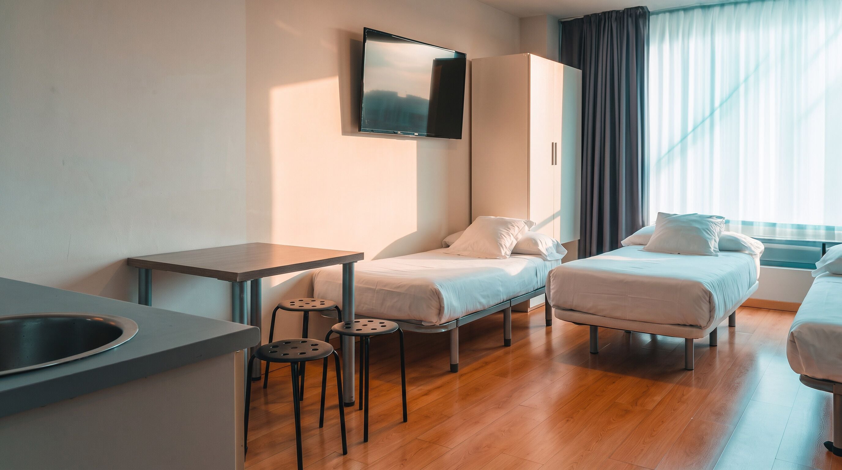 A hotel room with a bed, a desk, a chair, a TV, and a window with curtains.