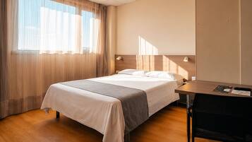 A hotel room with a bed, a desk, and a window with curtains.