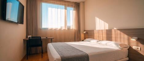 A hotel room with a bed, a desk, a chair, and a television.