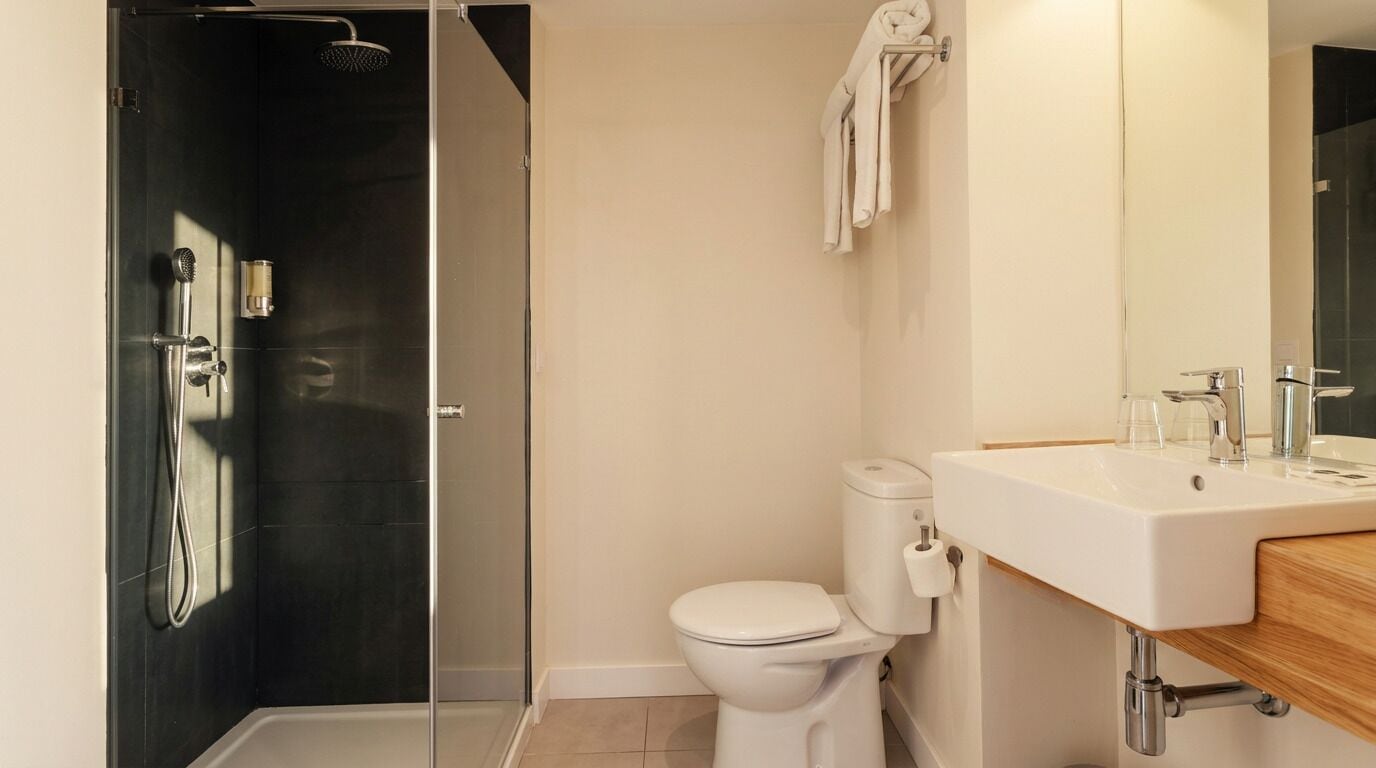 A modern bathroom with a glass shower enclosure, a white toilet, and a sink with a mirror.
