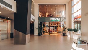 A modern food court with a 'FOODS SPACE' sign, featuring a variety of seating areas and a visible elevator.