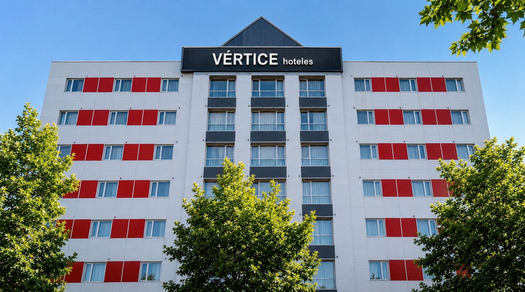 Un edificio de hotel de varios pisos con un cartel que dice 'VERTICE hotels' en la parte superior.