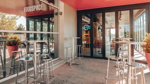 An outdoor seating area with metal bar stools and a red awning labeled "FOODSPACE."