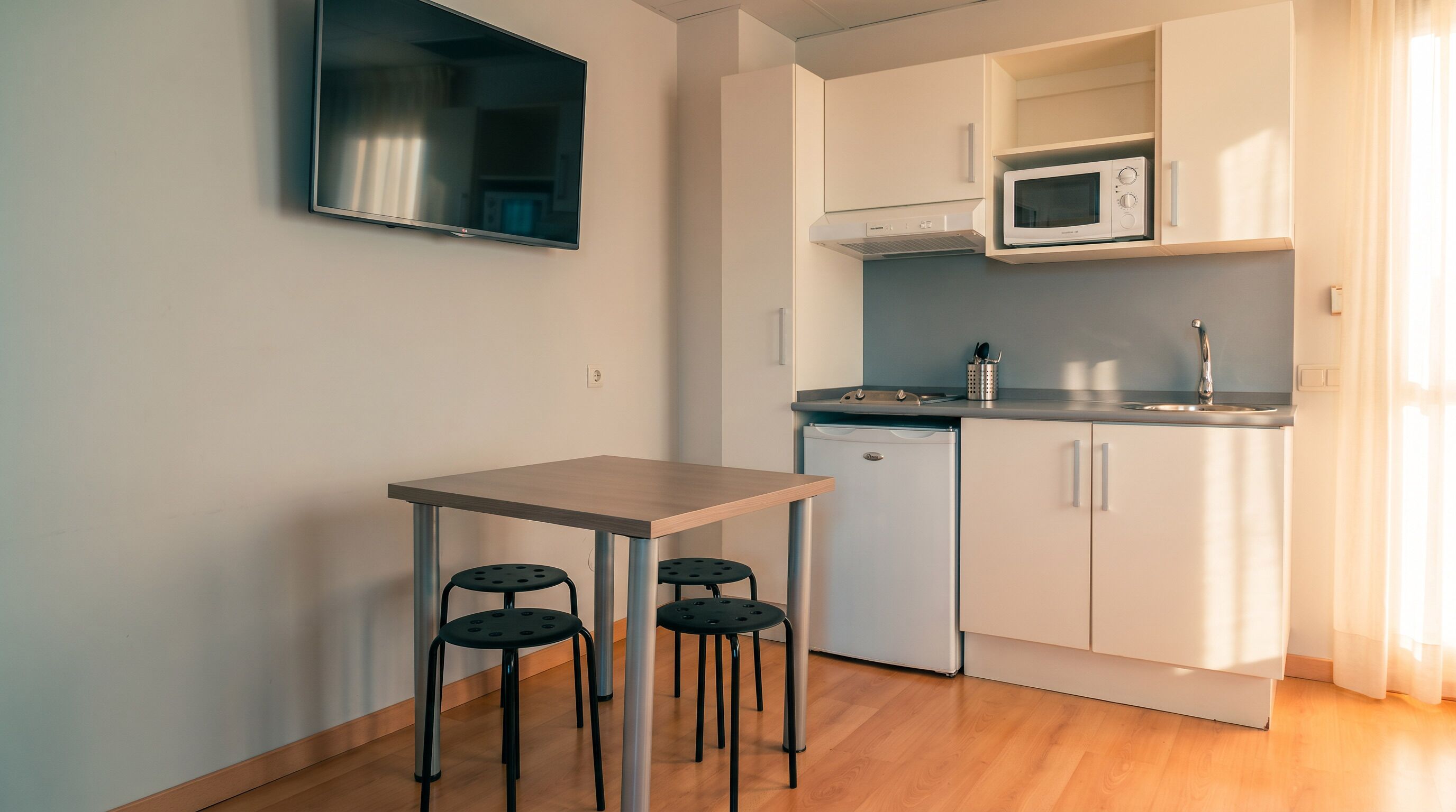 Una cocina funcional con microondas, fregadero y una pequeña mesa con taburetes.