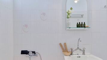 A bathroom with white tiles, a shower, a sink with a mirror, and a shelf with toiletries.