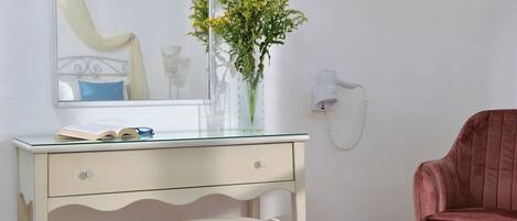 A room with a white desk, a chair, a vase with flowers, a mirror, a telephone, and a red chair.