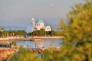 A coastal view with a prominent white building with blue domes, a beach, and a body of water. - Vasilaras Hotel (Agistri)