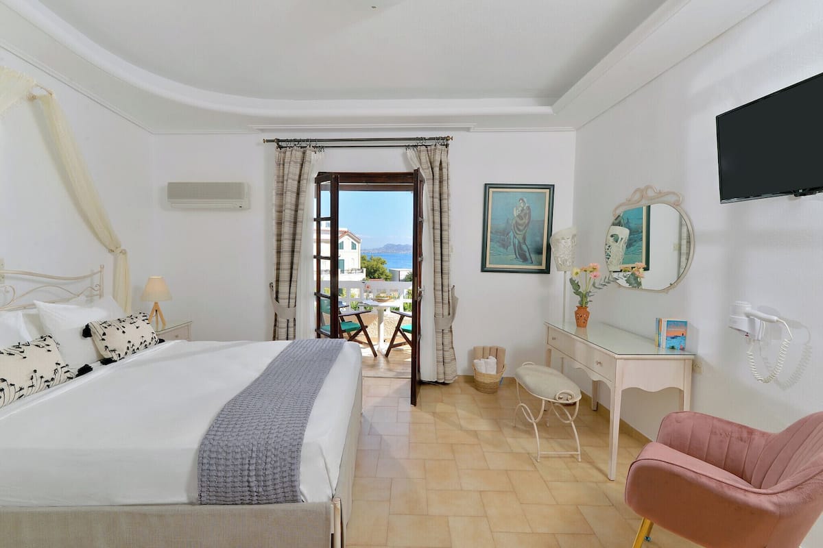 Habitación de hotel con cama, escritorio, silla, televisor y vistas al exterior.