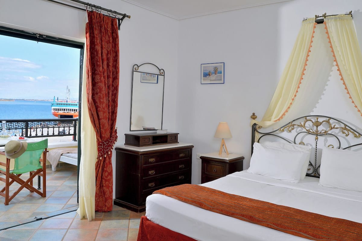 Habitación de hotel con cama, cómoda, silla, una mesita y vista al mar.