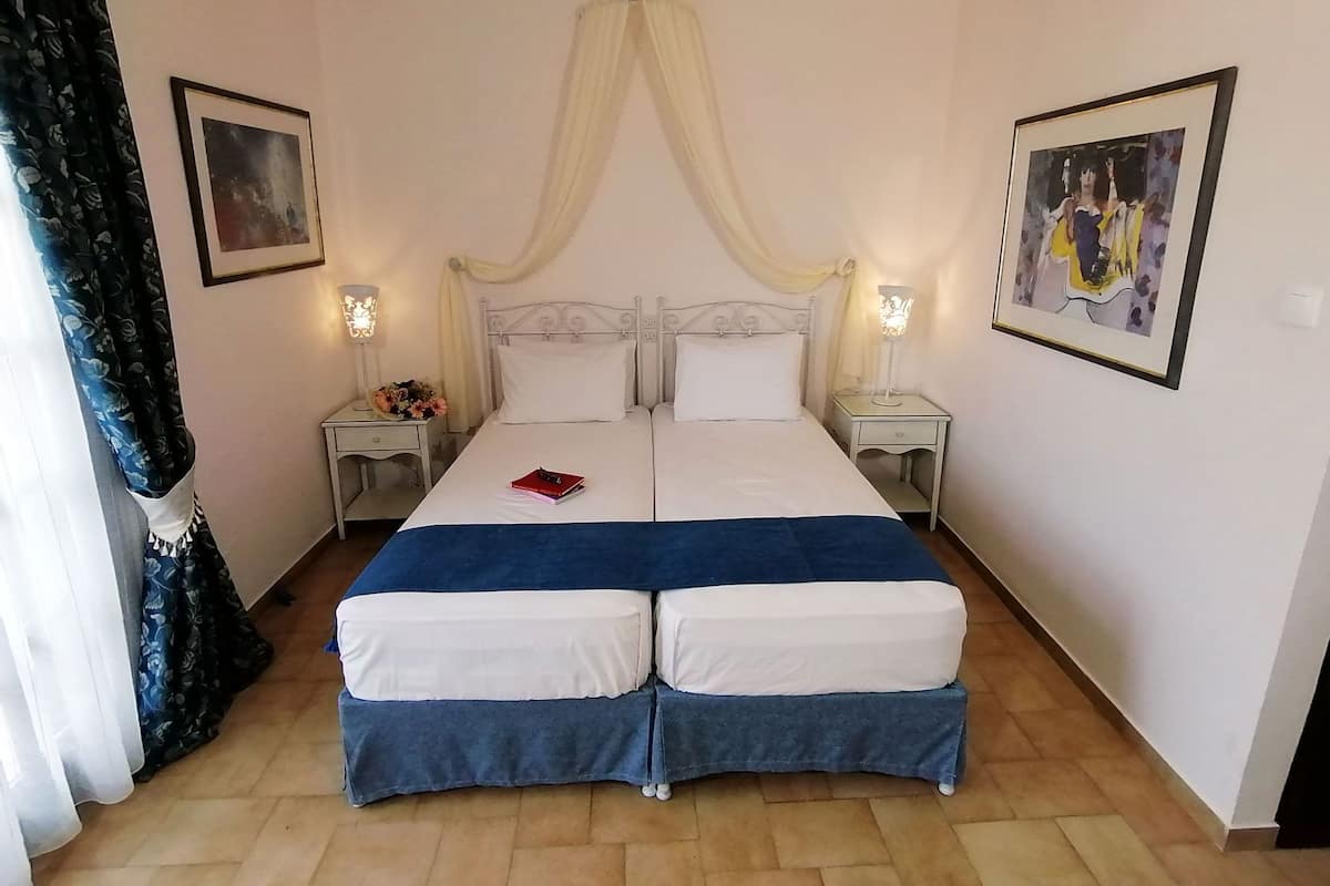 Una cama doble con ropa de cama blanca y azul, dos mesitas de noche con lámparas y un dosel sobre la cama.