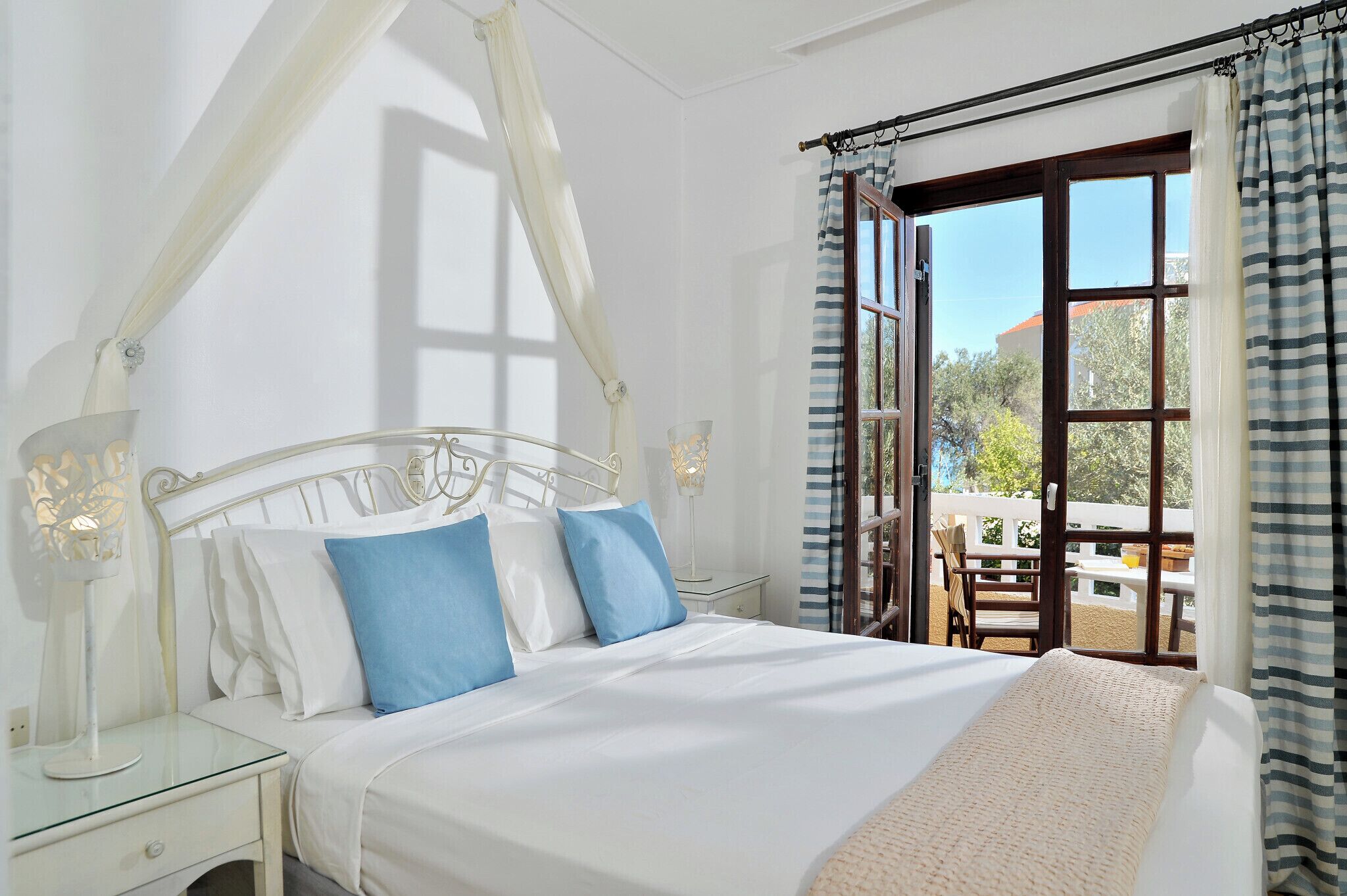 Una camera da letto con un letto a baldacchino bianco, un comodino e vista sull'esterno attraverso una grande finestra.