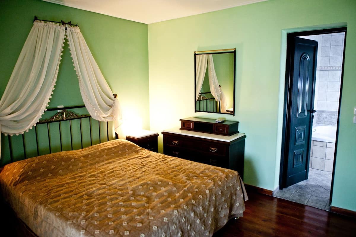 Un dormitorio con cama, mesitas de noche, cómoda, espejo y una puerta que da al baño.