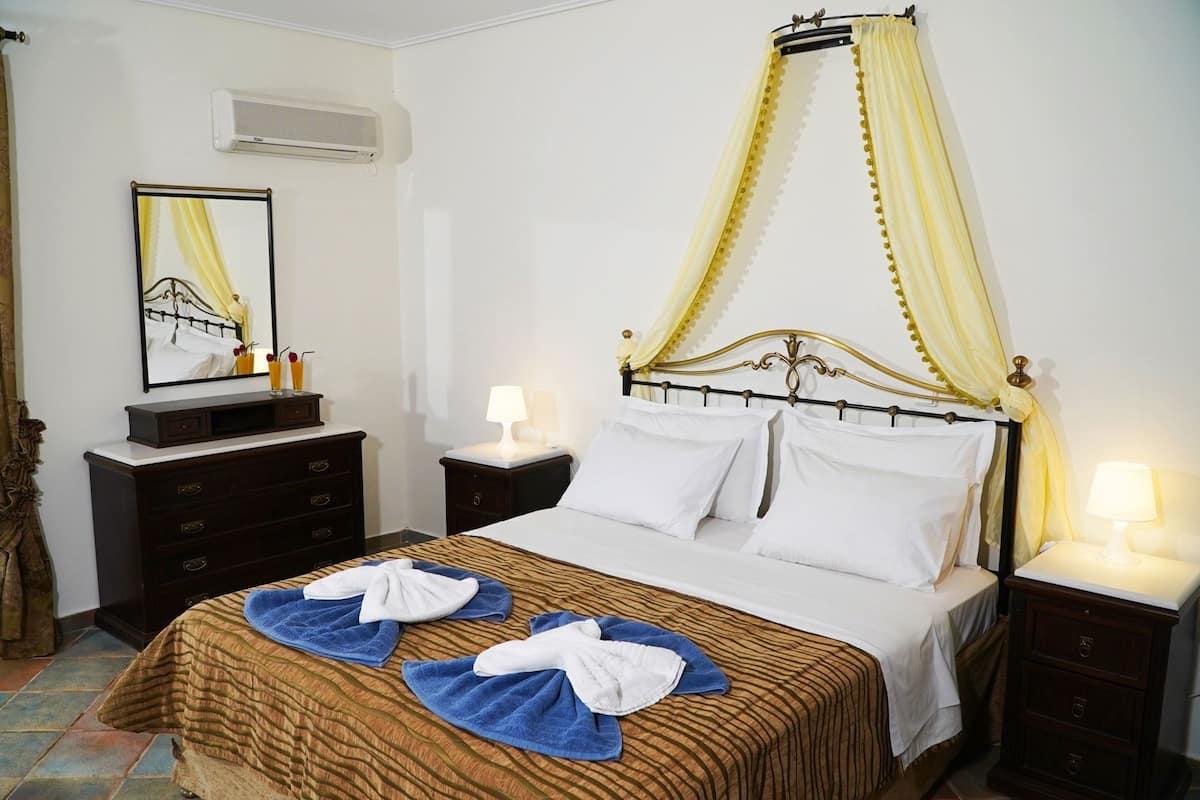 Habitación de hotel con cama, mesita de noche, cómoda, espejo y ventana con cortinas.