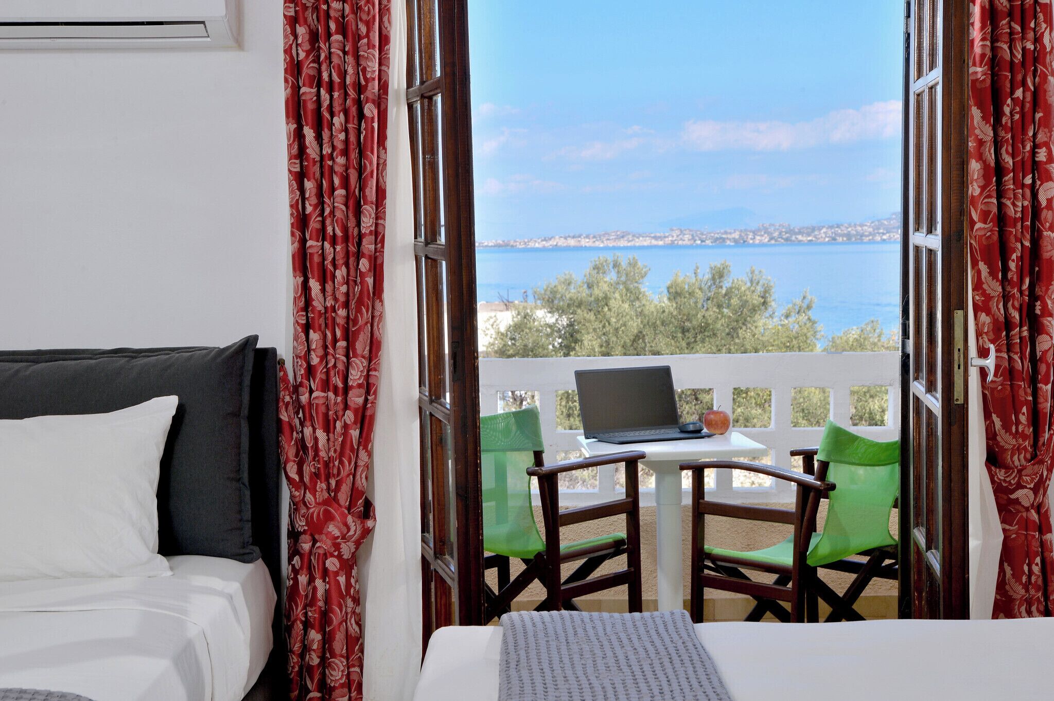 A room with a bed, a laptop on a small table, and a view of the sea.