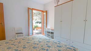 A bedroom with a bed, a chair, a wardrobe, and a sliding door leading to an outdoor area. - Casa Luppoli (Portoferraio)