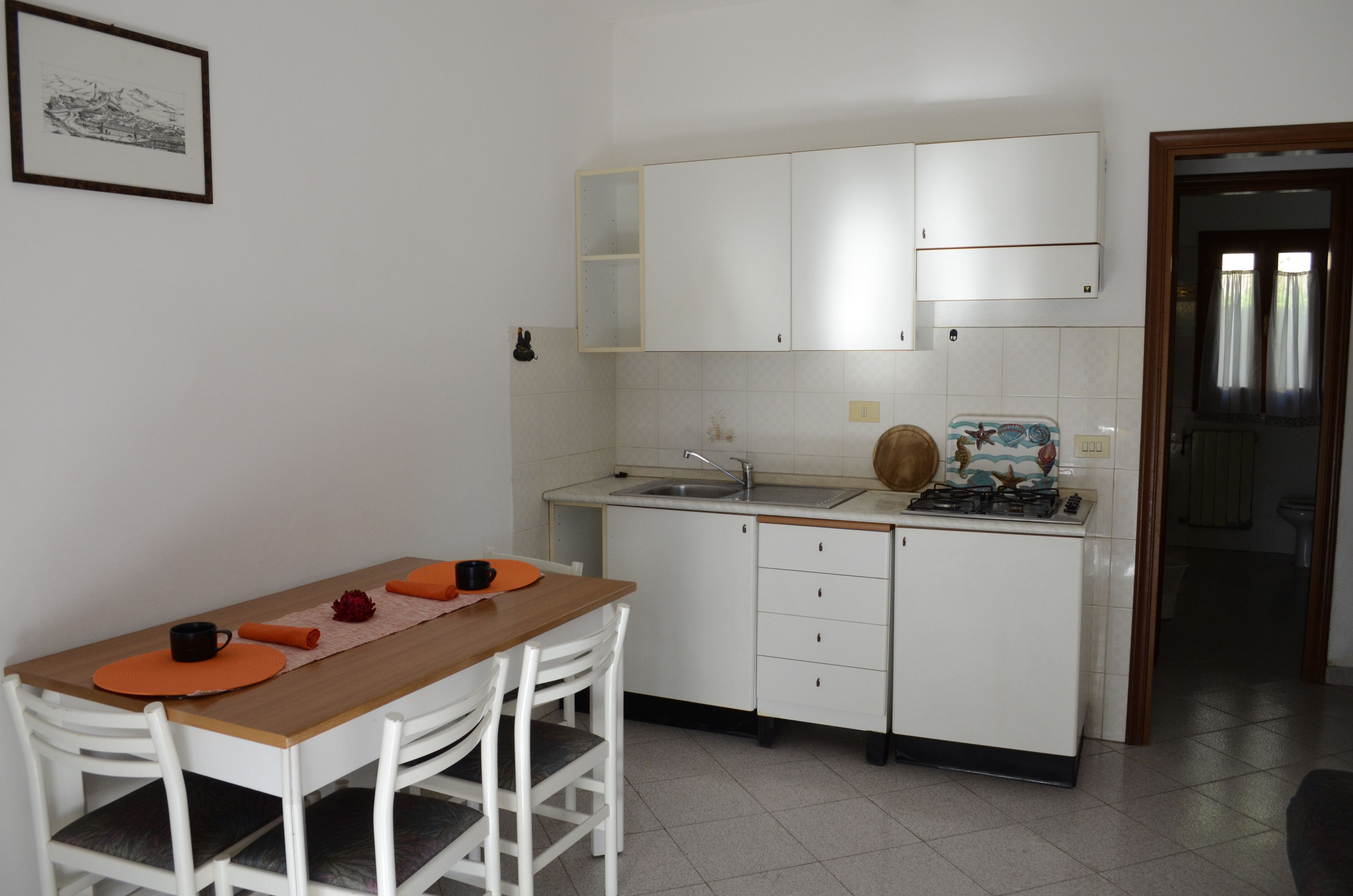 A compact kitchen with white cabinets, a wooden dining table, and a small countertop with a sink and stove.