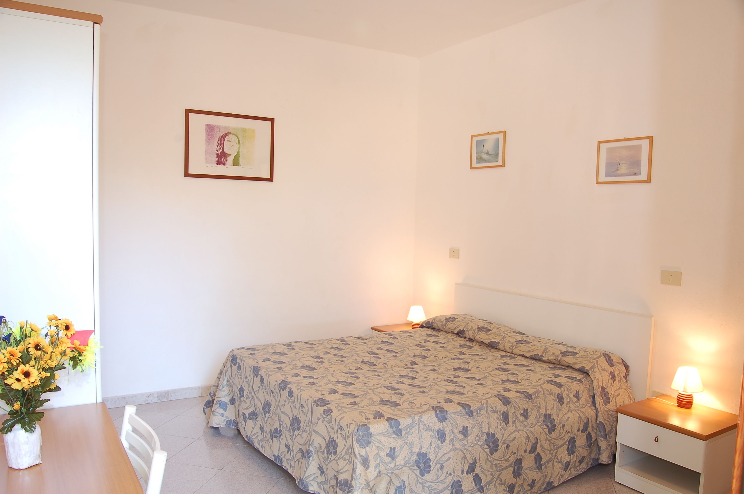 A bedroom with a bed, bedside tables, a lamp, a chair, and a table with flowers.