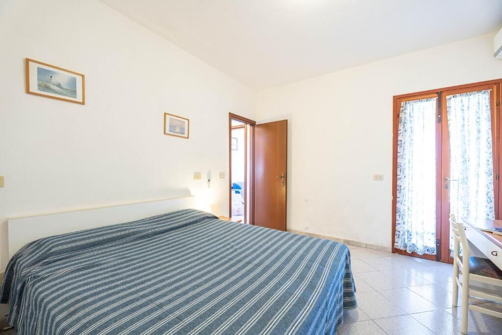 A bedroom with a bed, a desk, and a door leading to another room.