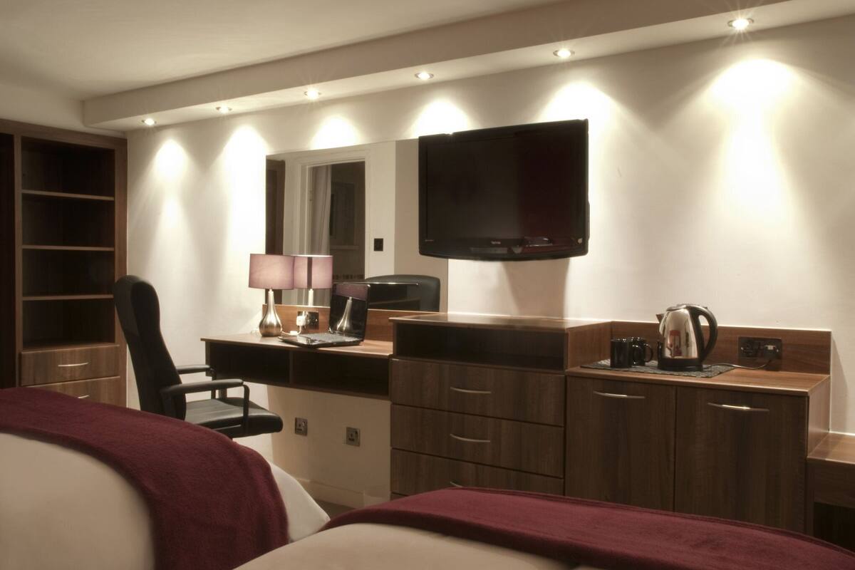 A hotel room with a bed, a desk with a lamp, a television, and a coffee maker.