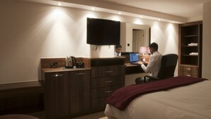 Quarto de hotel com cama, escrivaninha, computador, televisão e guarda-roupa.
