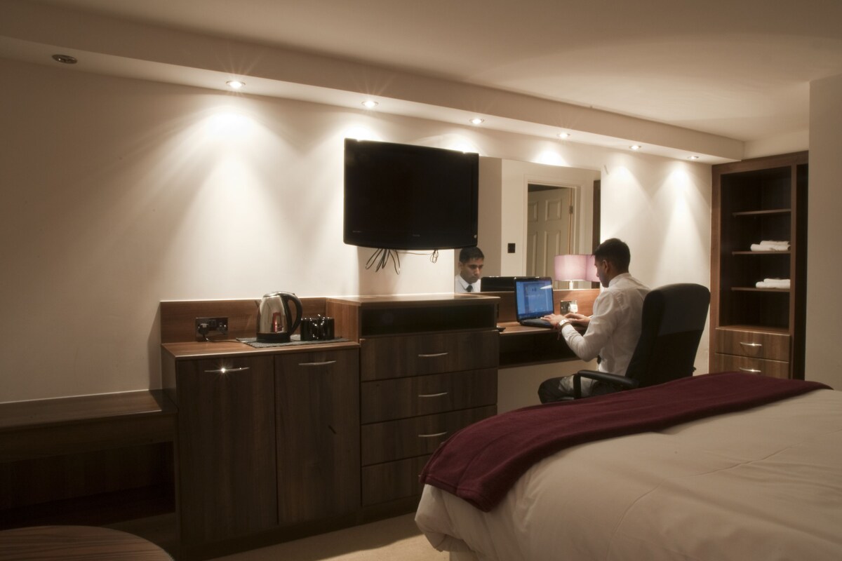 A hotel room with a bed, a desk with a computer, a television, and a wardrobe.