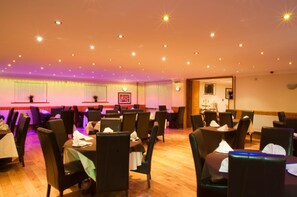 A dining area with tables and chairs, warm lighting, and a mirror on the wall. - Haveli Hotel (Pontyclun)