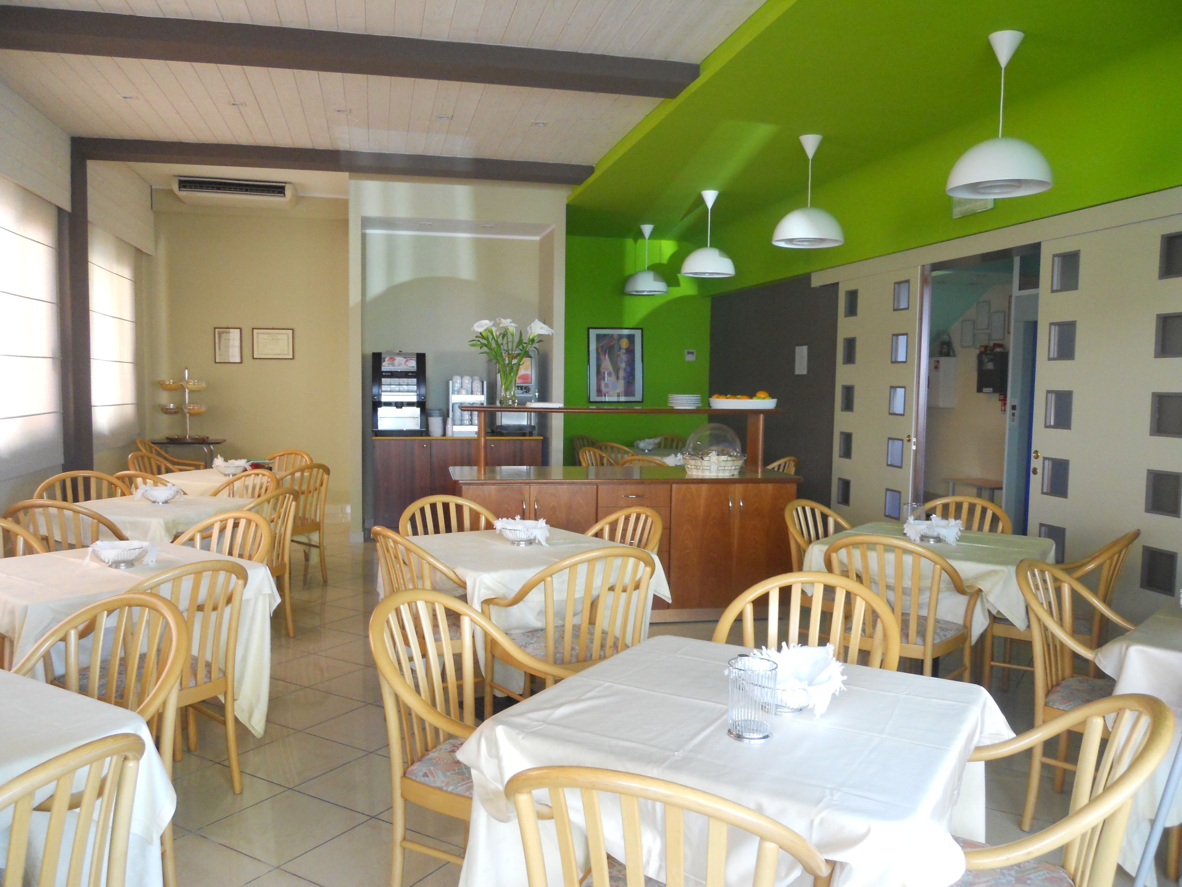 Un ristorante con sedie e tavoli di legno, un bancone con una cassa e una parete verde decorativa.
