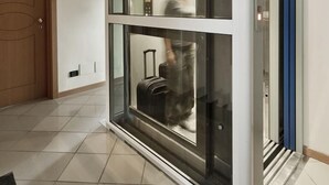 A modern hotel lobby with a glass elevator, a wooden door, and a tiled floor. - Hotel Ostuni (Rimini)