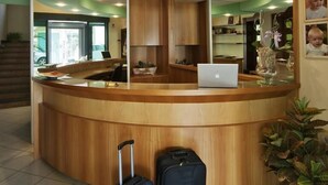 A reception area with a curved wooden desk, a laptop, and two suitcases. - Hotel Ostuni (Rimini)