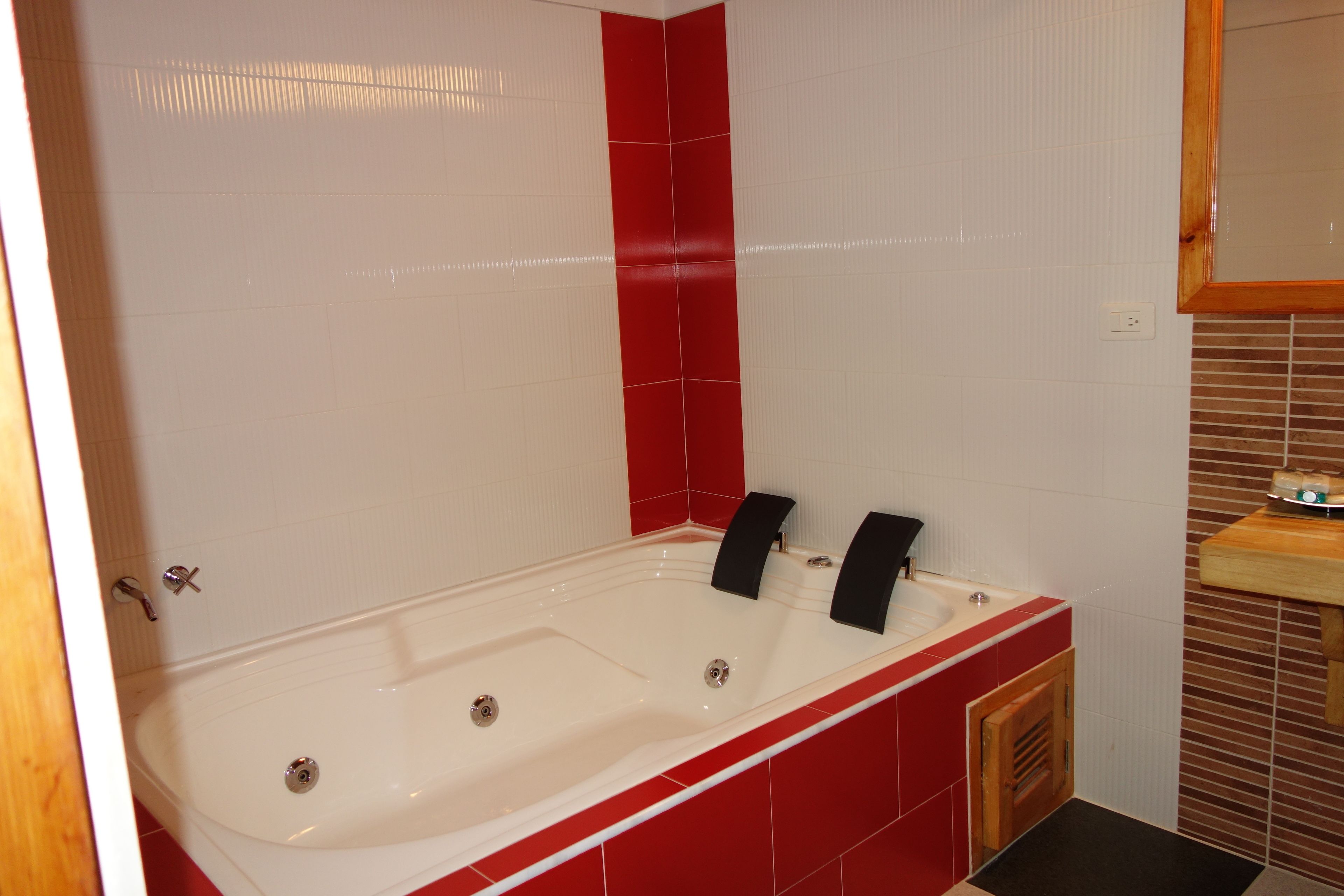 A bathroom with a white bathtub, red accents, and a wooden vanity.