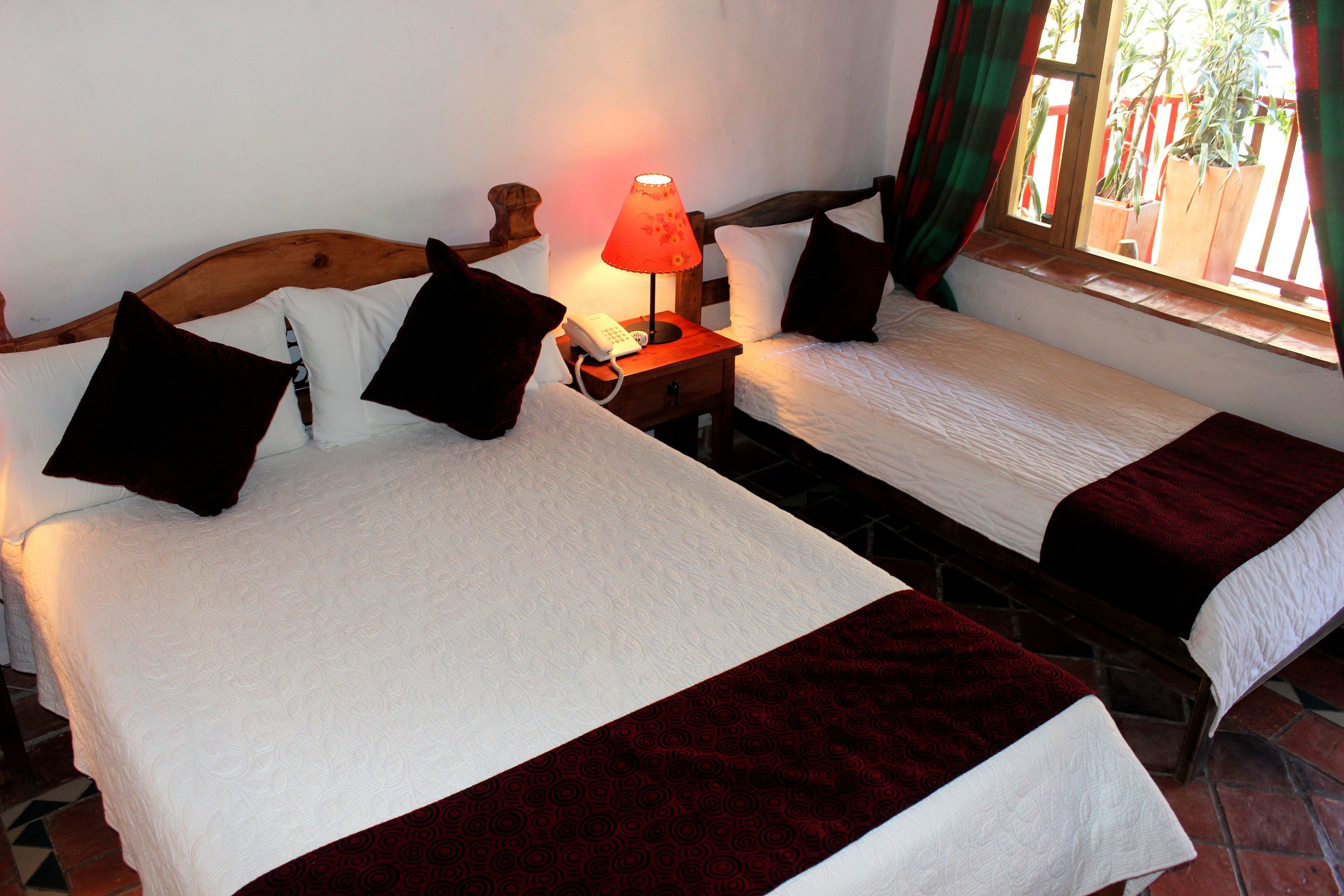 A double bed with a wooden headboard, a bedside table with a lamp, and a window with curtains.