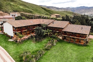 Un hotel con varias construcciones, cada una con tejado de baldosas y balcones. La propiedad está rodeada de exuberante vegetación y colinas al fondo.