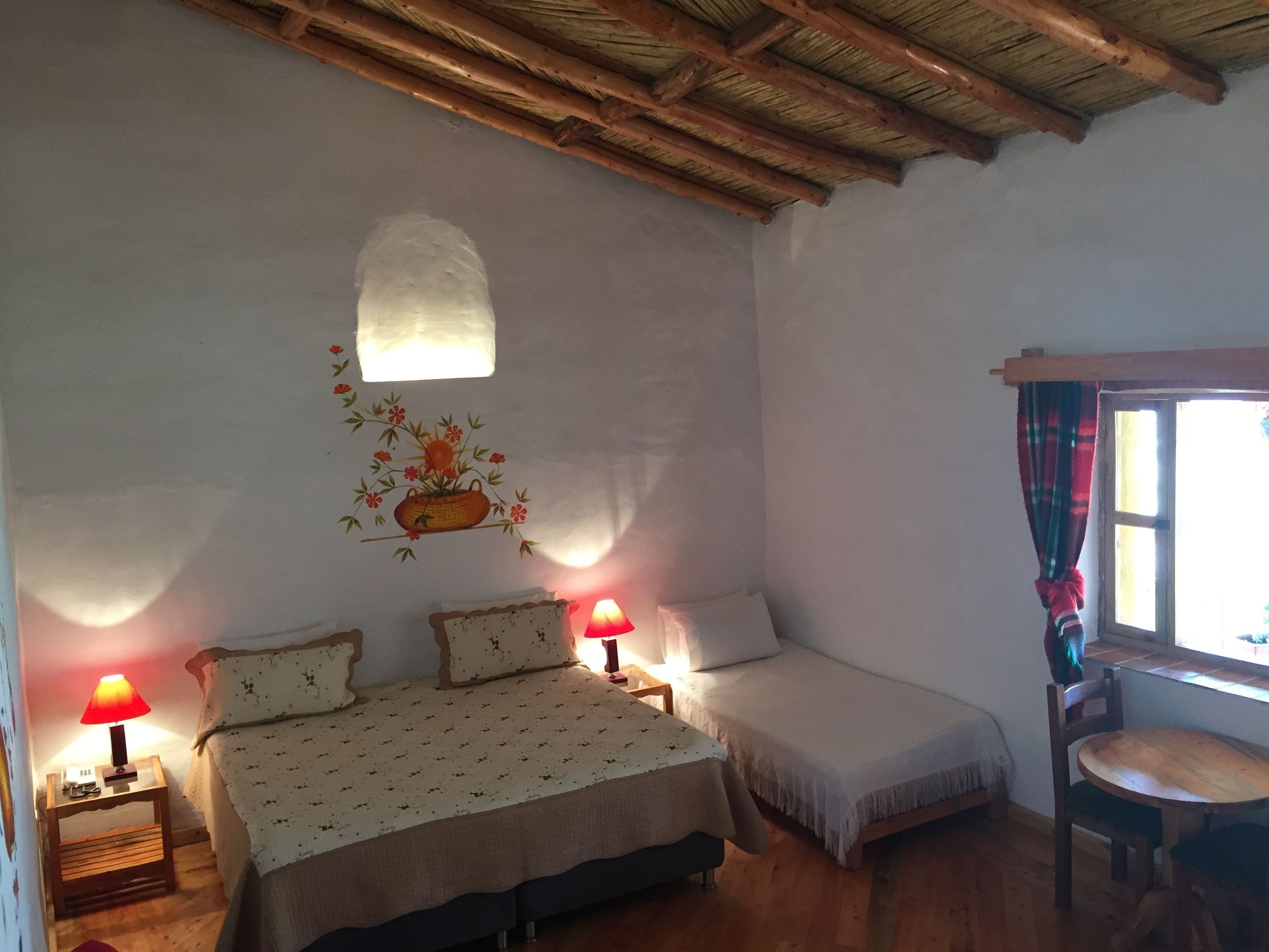 A bedroom with a bed, two bedside tables with lamps, a small table, and a window with curtains.