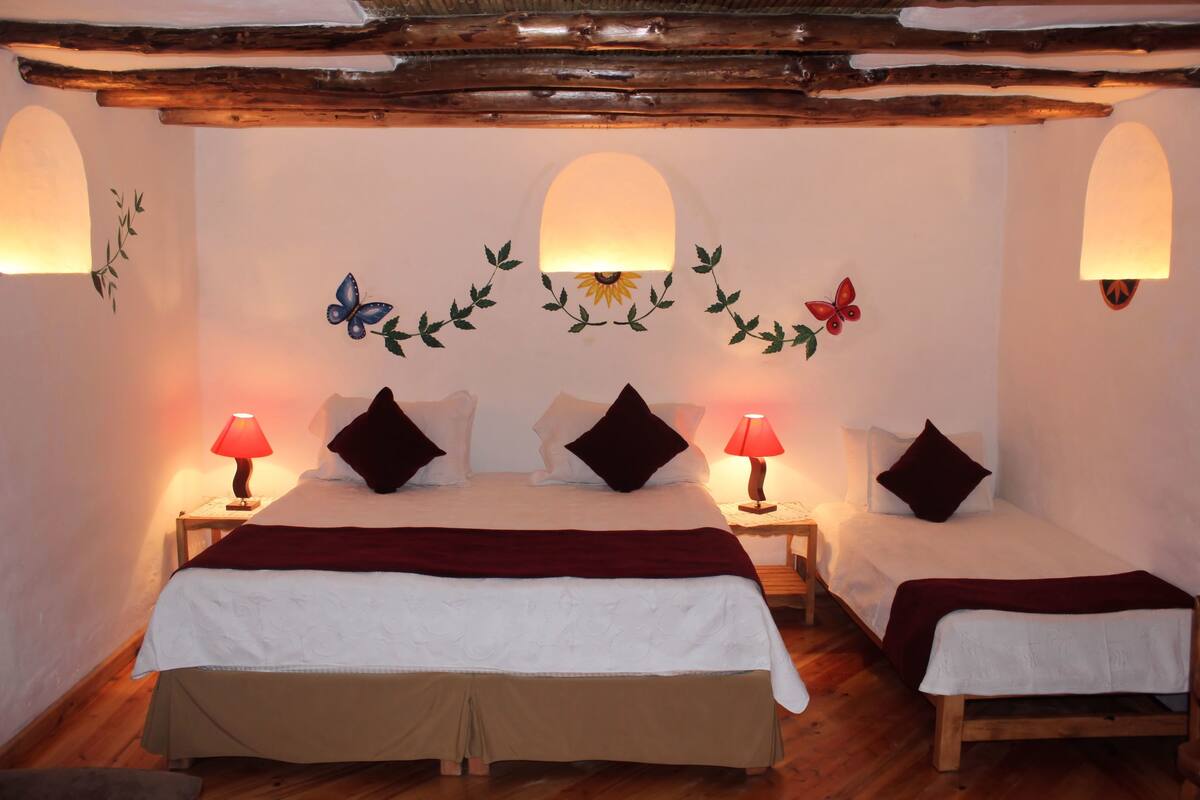 A room with two beds, each with a red lamp, a floral wall decoration, and a wooden ceiling.