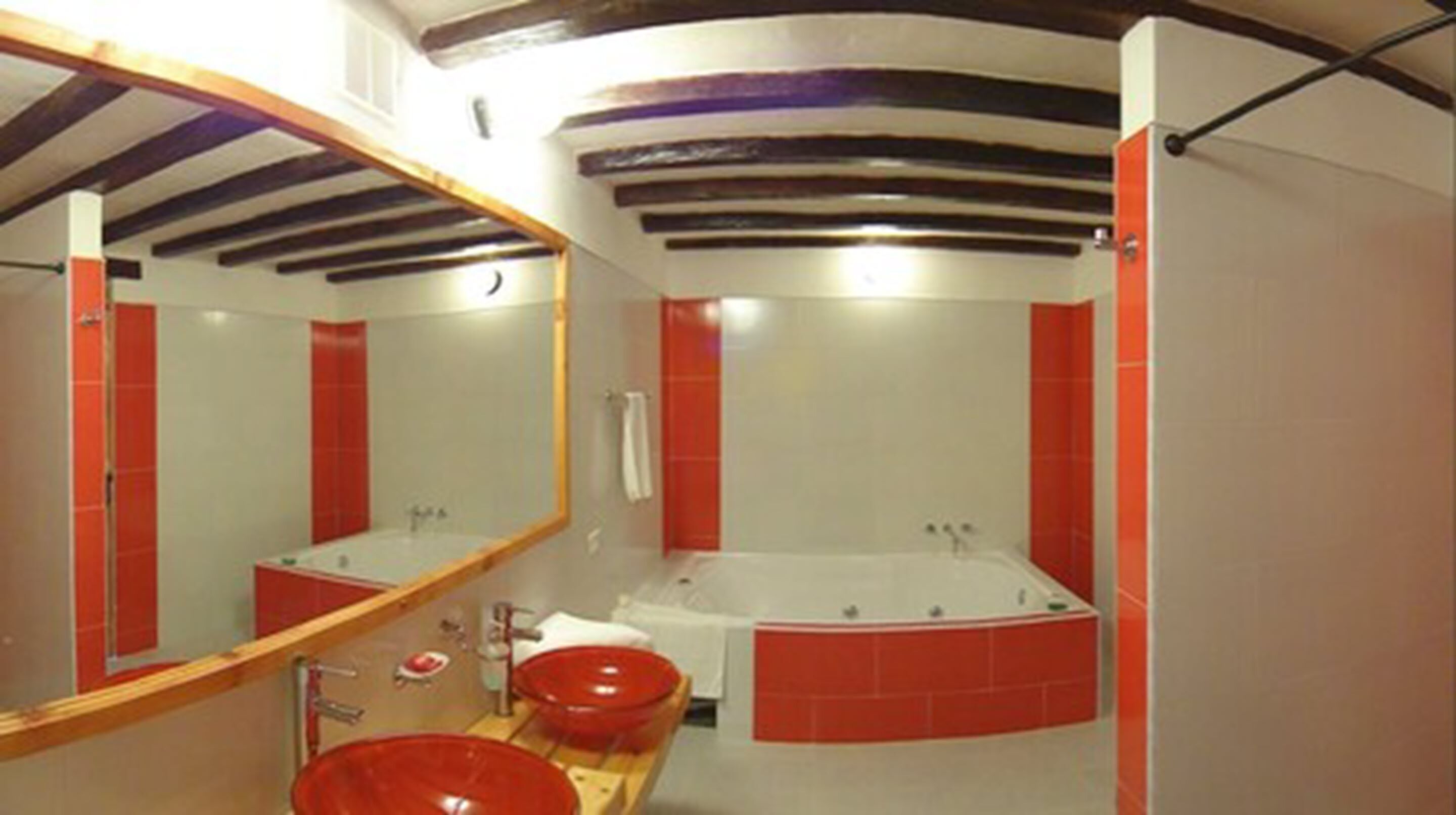Un baño con un espejo grande, una bañera y un lavamanos rojo.