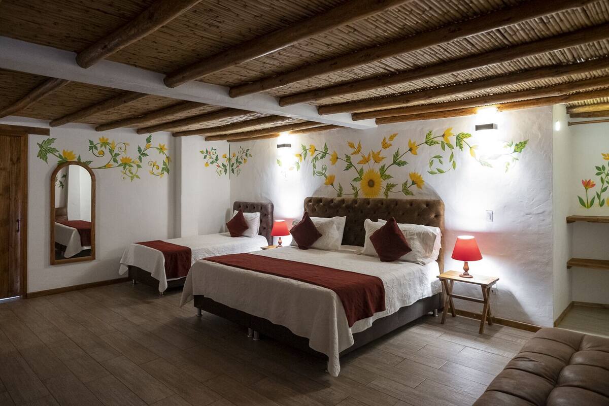 A room with two beds, wooden beams on the ceiling, and floral wall decorations.