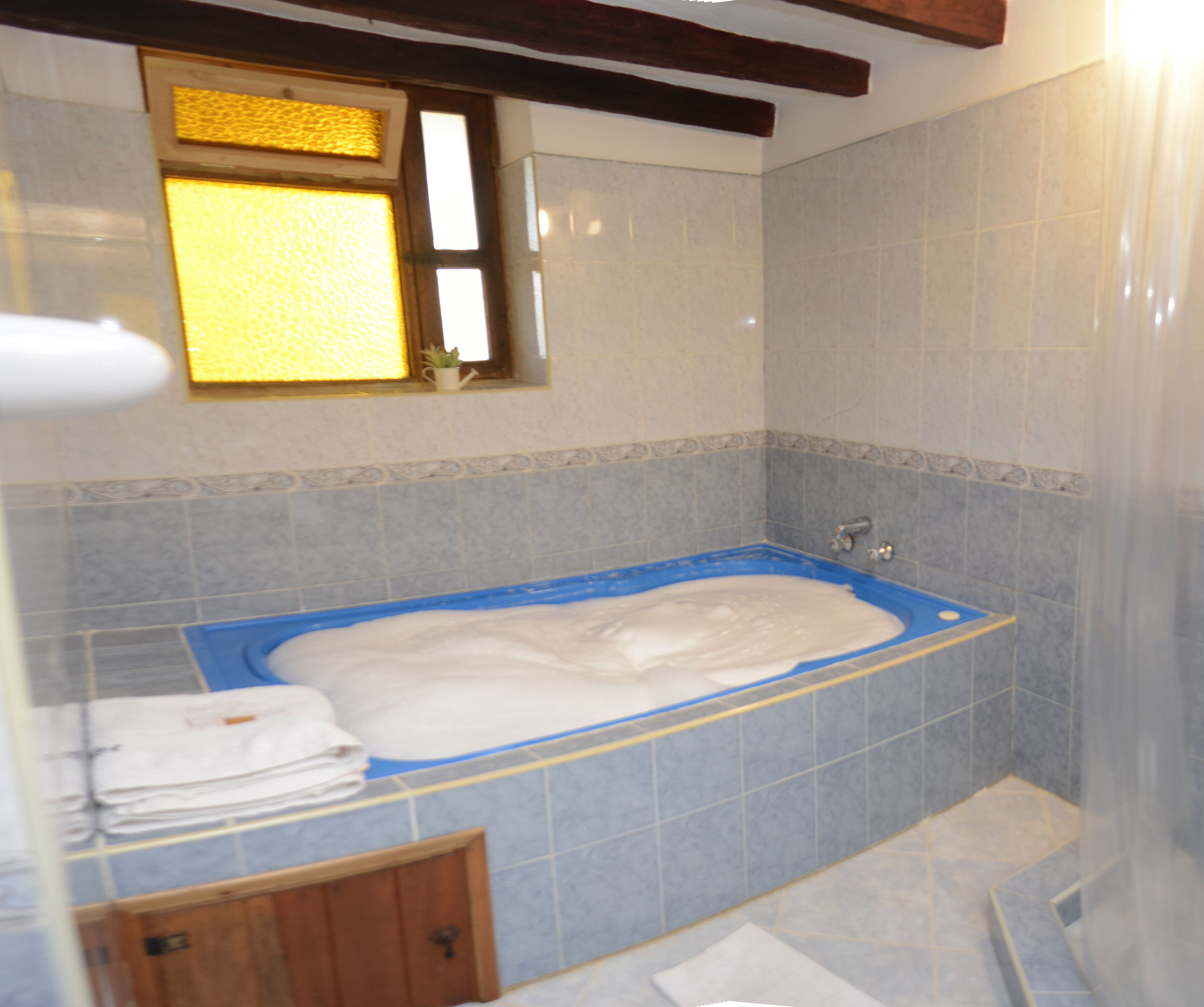 A bathroom with a bathtub, tiled walls, a window, and a wooden door.