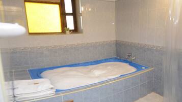 Un baño con bañera, paredes de azulejos, una ventana y una puerta de madera.