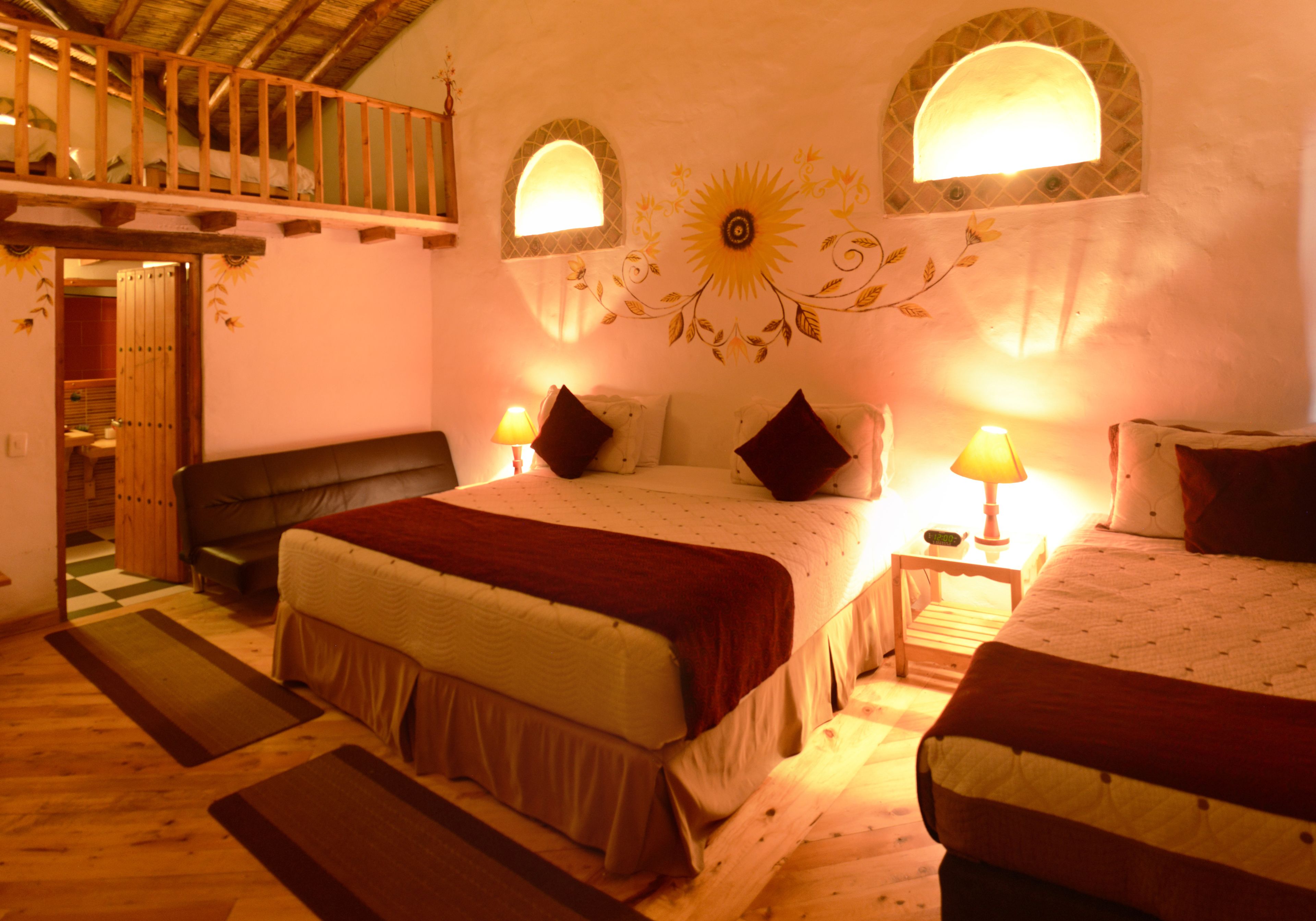 A bedroom with a large bed, two bedside tables with lamps, a wooden bench, and a balcony.