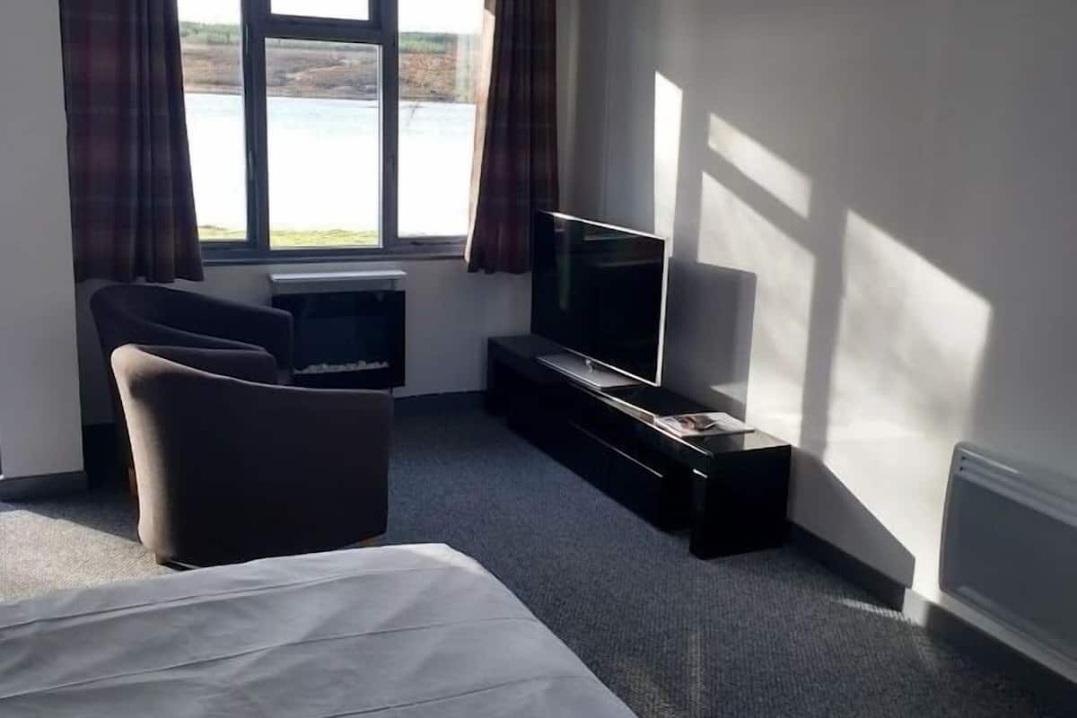 A hotel room with a bed, a TV, a chair, and a window with curtains.