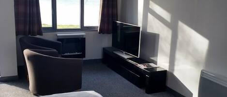 A hotel room with a bed, a TV, a chair, and a window with curtains.