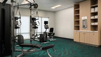 A fitness center with cardio machines, weight benches, and a wall-mounted water dispenser.