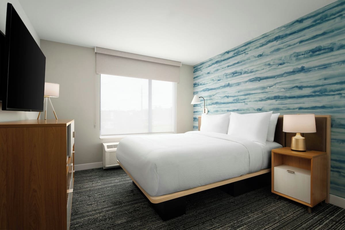 A hotel room with a bed, a desk, a TV, a lamp, and a window.