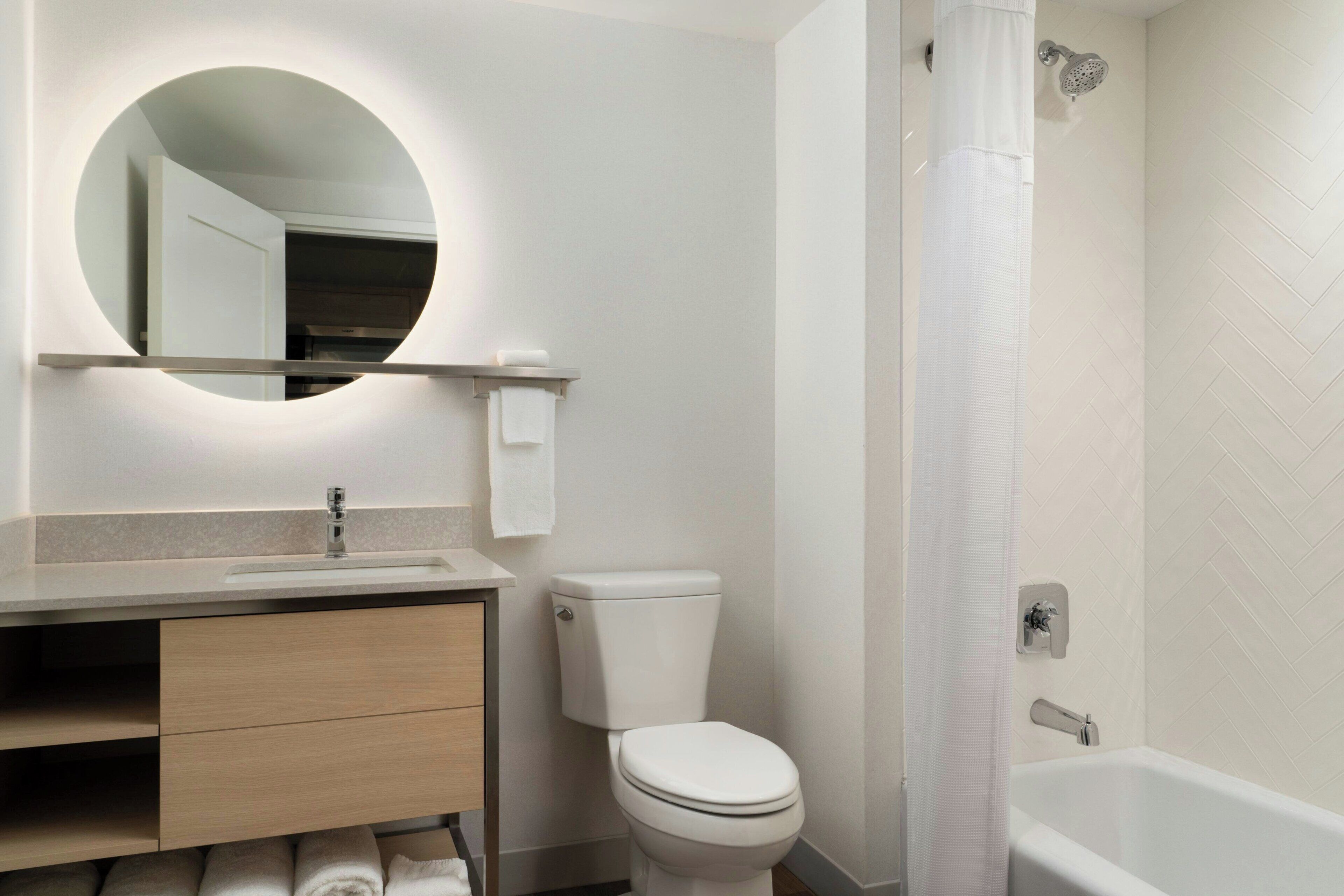 Un baño moderno con un espejo redondo, inodoro, lavamanos y bañera.