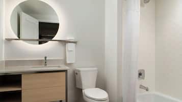 Un baño moderno con un espejo redondo, inodoro, lavamanos y bañera.