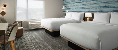 A hotel room with two beds, a desk, chairs, a window, and a wall with a blue pattern.