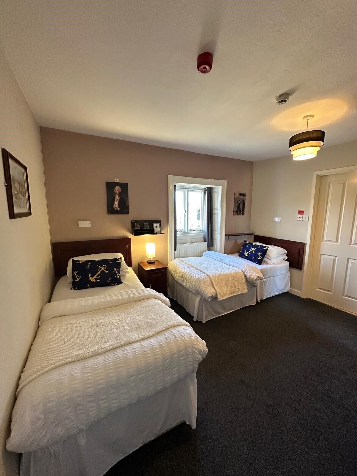 A hotel room with two beds, a window, a door, and a ceiling light.