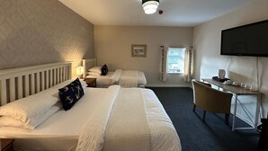 A hotel room with two beds, a desk, a television, and a window with curtains.