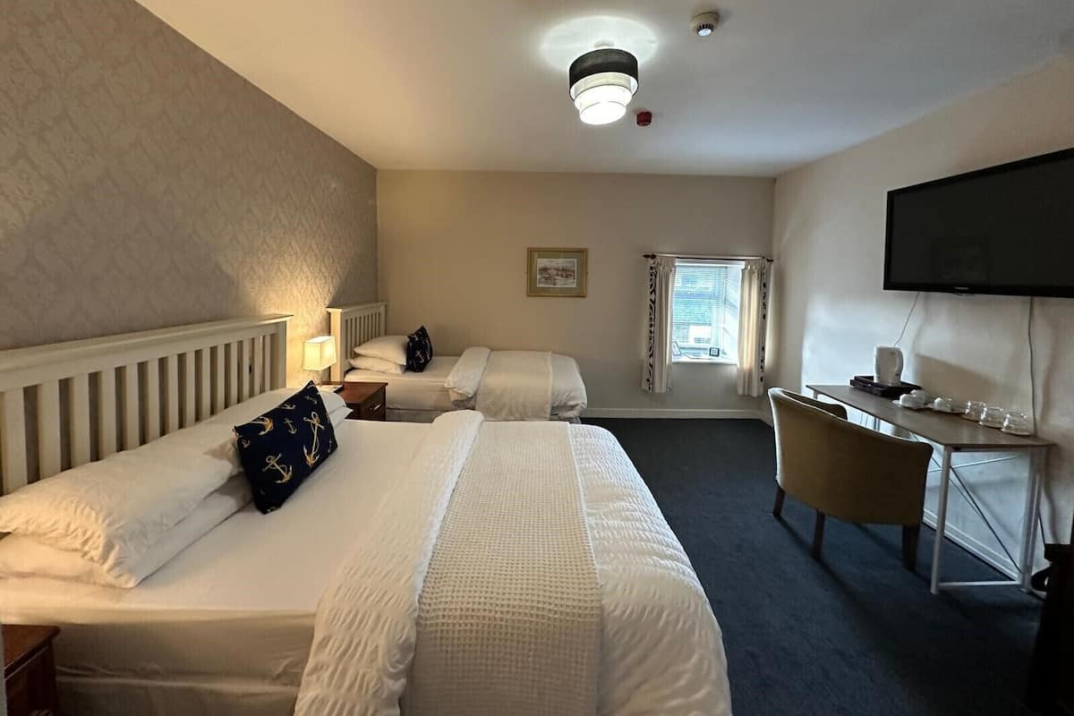 A hotel room with two beds, a desk, a television, and a window with curtains.