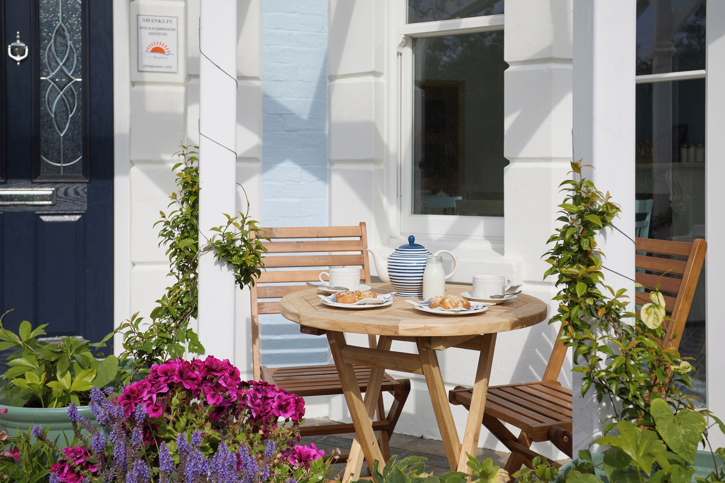 An outdoor seating area with a table set for two, featuring a teapot, cups, and pastries.